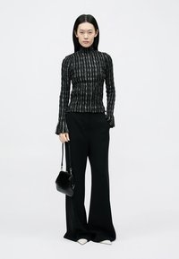 Black ribbed turtleneck top with vertical white stripes, paired with wide-leg black pants and a small black structured handbag.