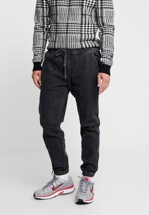 Zwarte denim joggers met elastische boorden, een trekkoord in de taille en een relaxte pasvorm, gecombineerd met een zwart-wit gestreepte top met lange mouwen.