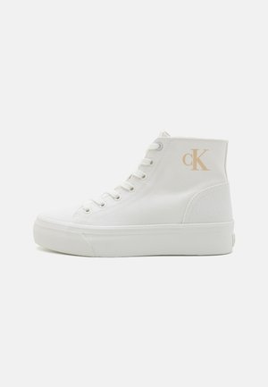 Baskets montantes blanches en toile avec une semelle blanche plate et un détail de logo beige. Elles possèdent des lacets et une tige texturée.