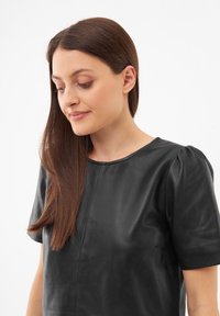 Musta nahkatoppi pyöreällä pääntiellä, lyhyillä puffihihnoilla ja sileällä pinnalla. Edessä on sauma, joka tuo muotoiluun lisäyksityiskohtia.