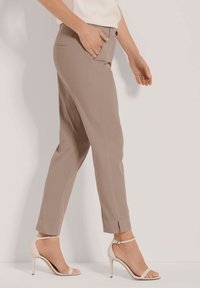 Beige op maat gemaakte broek met een slim fit, voorzien van een tailleband en zijzakken. Gecombineerd met lichtgekleurde open teenhakken.