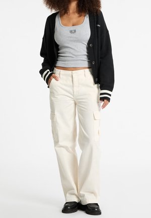 Black cardigan with white stripes, gray tank top, cream cargo pants with side pockets, and black chunky shoes. Casual layered outfit.