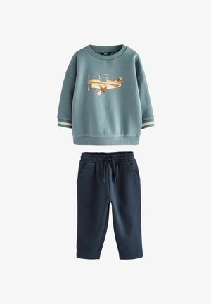 Šviesiai mėlyna sportinė pagalvėlė su lėktuvo siuvinėjimu, apvalus apykaklė, įtempti rankogaliai; tamsiai mėlynos jogger kelnės su elastine juosta ir šoninėmis kišenėmis.