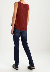 Bordeaux ærmeløs bluse med en nøglehul-detail bagpå, lagdelt kant, parret med mørkeblå jeans og sorte sko.