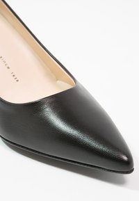 Chaussure plate en cuir noir à bout pointu avec doublure intérieure beige et texture subtile sur fond blanc.