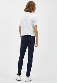 Vit kortärmad t-shirt kombinerad med mörkblå skinny jeans. Jeansen har hög midja och diskret sömnad på bakfickorna.