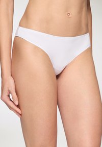 Bikini in cotone bianco con texture liscia, design a vita bassa e copertura minima, dotato di un elastico in vita e aperture delle gambe senza cuciture.
