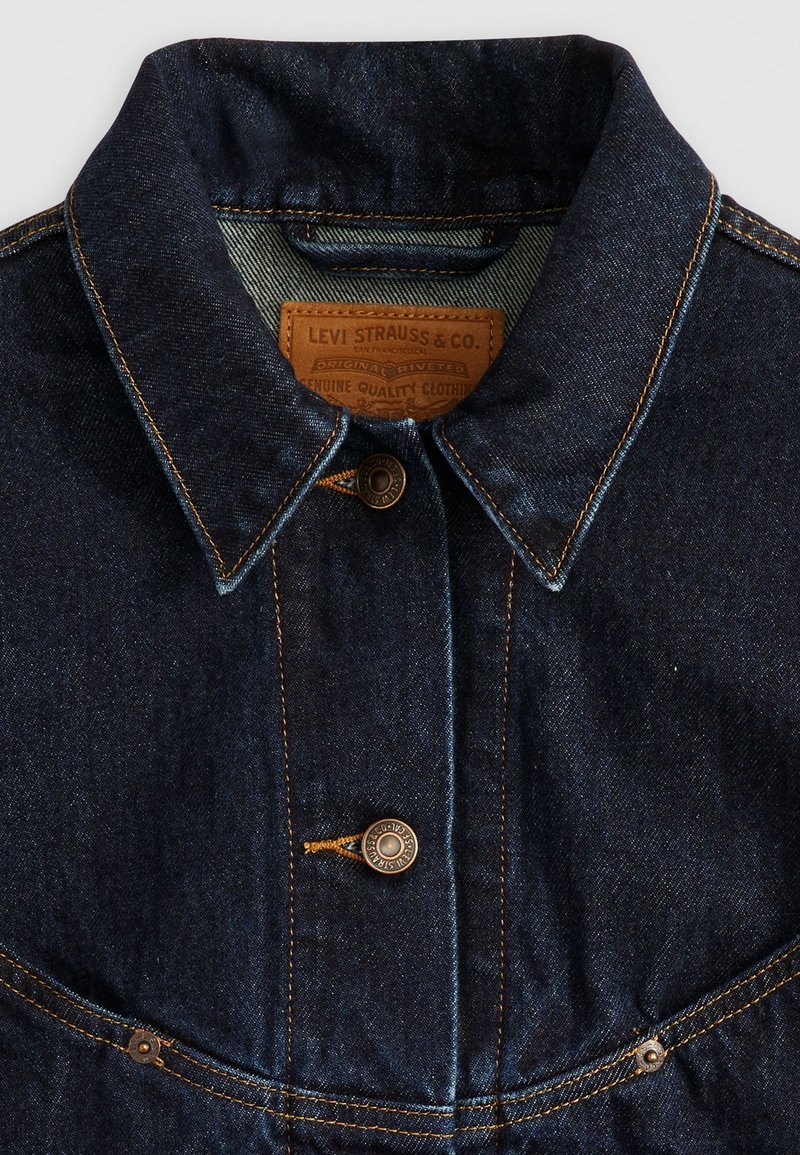 Giubbotto in denim blu scuro con colletto, chiusura con bottoni di rame e cuciture in contrasto. Etichetta in pelle cucita all'interno del colletto.