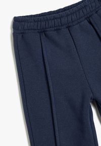 Marineblå joggers lavet af blødt stof, med elastisk talje og to plisseringer foran for en afslappet pasform.