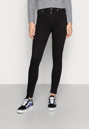 Sort højtaljede skinny jeans med frynsede kanter, parret med sorte og blå sneakers med snørebånd og suede-detaljer.