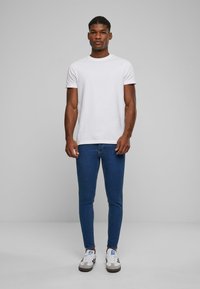 Camiseta blanca de cuello redondo, jeans ajustados azul y zapatillas blancas con acentos en gris y azul. Textura suave y diseño ajustado.