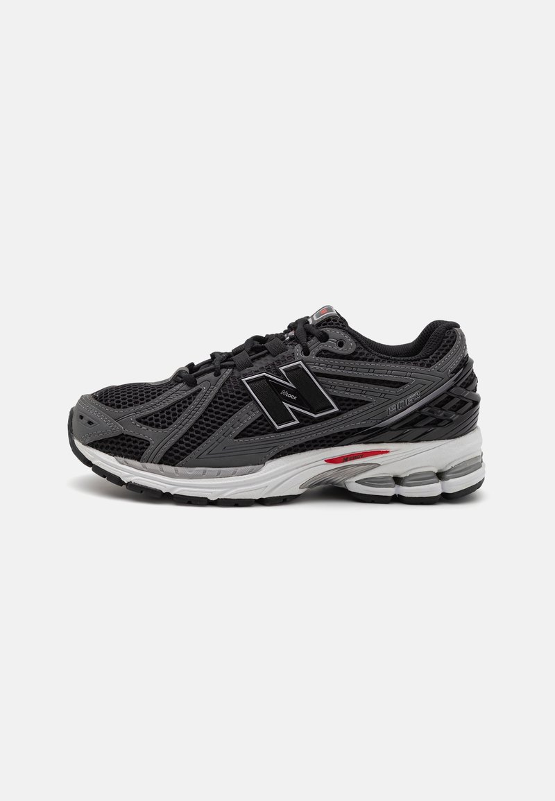 Chaussure de course athlétique noire et grise avec tige en mesh, grand logo "N" sur le côté, semelle blanche et grise rembourrée, et lacets noirs.