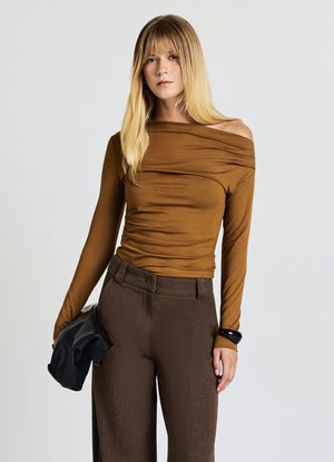 Top marrone a maniche lunghe con spalle scoperte e dettagli arricciati, abbinato a pantaloni a vita alta testurizzati marrone scuro e una pochette nera.