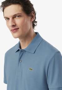 Koszulka polo z krótkim rękawem w jasnoniebieskim kolorze, wykonana z teksturowanej tkaniny, z dwoma guzikami przy kołnierzyku oraz haftowanym logo krokodyla na piersi.