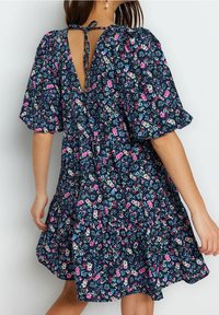 Kwiatowa sukienka z ciemnoniebieskiego materiału, z krótkimi bufiastymi rękawami, głębokim dekoltem w tylnej części z wiązaniem oraz falbaniastej spódnicy z wielokolorowymi wzorami kwiatowymi.