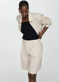Ljus linneskjorta i krämfärgad över en svart topp, tillsammans med beige skräddarsydda shorts. Har en avslappnad passform och detaljerad sömnad.