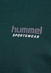 Grønt stof med 'hummel SPORTSWEAR' logo trykt i gråt og hvidt tekst i midten.