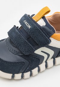 Sneakers blu navy realizzati in suede e pelle, con cinturini in velcro, suola texturizzata e un accento giallo sul tallone.