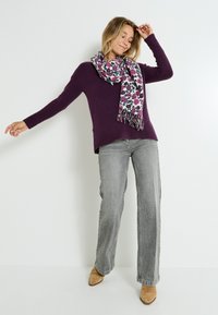 Suéter de punto morado combinado con una bufanda de patrón floral. Jeans de pierna ancha gris y zapatos de punta beige completan el atuendo.
