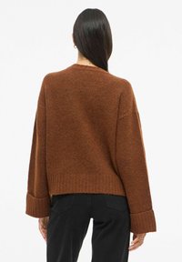 Pehmeast materjalist roostekarva kampsun, millel on lõdvestunud istuvus, soonilised mansetid ja lühendatud pikkus. Tagantvaates on näha minimaalset detailset kujundust.