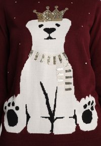 Maglione bordeaux con motivo di un orso polare bianco con una corona e dettagli in paillettes dorate, accentuato da impronte di zampa e fiocchi di neve.