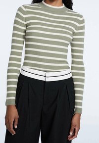 Geribbelde gebreide top met lange mouwen in het groen met witte strepen, voorzien van een hoge kraag en gecombineerd met hoge zwarte broeken en een witte riem.