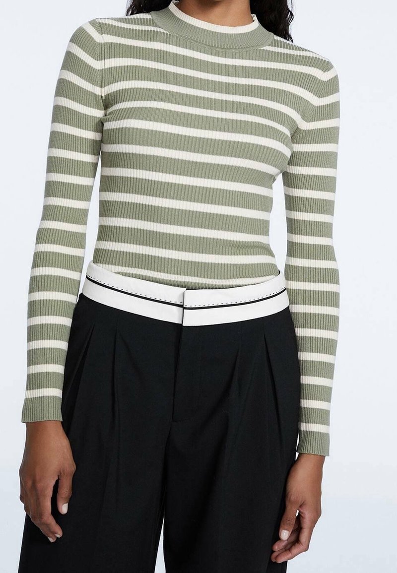 Geribbelde gebreide top met lange mouwen in het groen met witte strepen, voorzien van een hoge kraag en gecombineerd met hoge zwarte broeken en een witte riem.