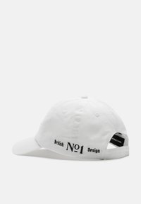 Een witte honkbalpet met een gebogen rand. Kenmerkt zich door zwarte tekst: "British N°1 Design" aan de zijkant. Gemaakt van katoen. Verstelbare band aan de achterkant.