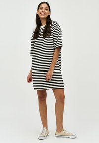 Svart och vit randig oversized t-shirtklänning med korta ärmar, sidoflikar och rund halsringning, och matchad med ljusa sneakers.