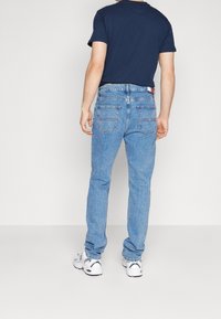 Blå denimjeans med rak passform, som har en design för bakfickor och en strukturerad tygkvalitet. Bärs med en marinblå t-shirt och sneakers.