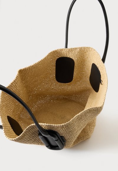 Sac fourre-tout beige tissé avec poignées et garniture en cuir noir, ouverture supérieure montrant un intérieur spacieux et un motif tissé texturé.