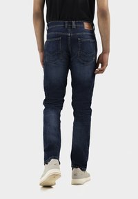 Dark blue denim jeans featuring a slim fit, five-pocket design, and subtle stitching accents on the back pockets.