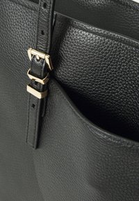 Zwarte leren handtas met een gestructureerde afwerking, voorzien van een gouden gesp en riemdetails. Het interieur toont een vak langs de rand.