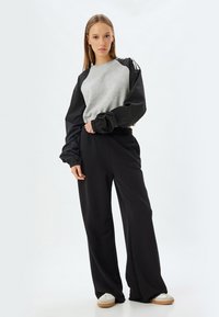 Grijze sweatshirt van jersey met zwarte, gepofte mouwen; gecombineerd met losse zwarte broek. Heeft elastische boorden en tailleband; casual ontwerp.