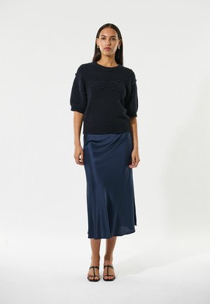 Navy gebreide trui met korte mouwen en gestructureerde bobbel-details, gecombineerd met een lange, elegante navy satijnen rok en zwarte strappy hakken.