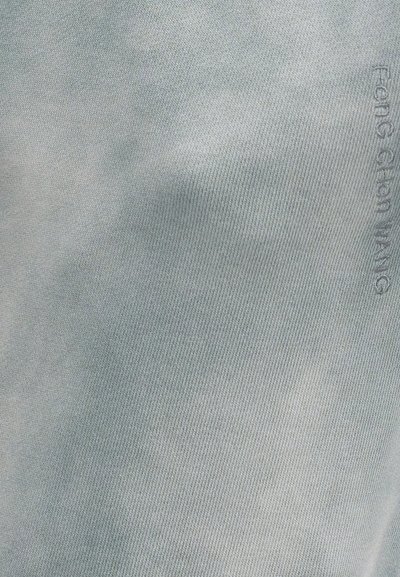 Ανοιχτό γκρι πλεκτό ύφασμα με λεπτό ανάγλυφο κείμενο "Feng Chen Wang" ραμμένο κατακόρυφα κοντά στην δεξιά άκρη.