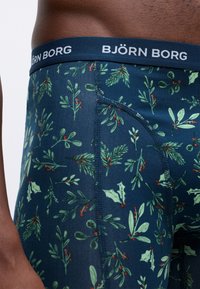 Tamsiai mėlyni boxeriai su botaniniu raštu, kuriame matosi žali ivyko lapai ir raudonos uogos. Su žymėta elastinga juosmens juosta.