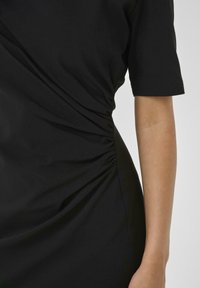 Black dress with short sleeves, gathered side detailing, smooth texture, and form-fitting silhouette. No visible hardware or patterns.