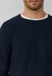 Marineblaues Langarm-Crewneck-Pullover aus strukturiertem Stoff, mit weißem Kragen und Raglanärmeln. Einfaches und funktionales Design.