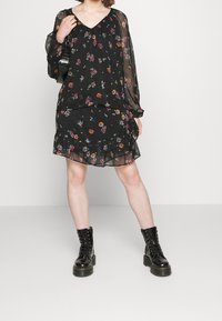 Vestido negro con flores, de mangas largas y transparentes, con detalles de volantes en capas, combinado con botas de combate negras con cordones.