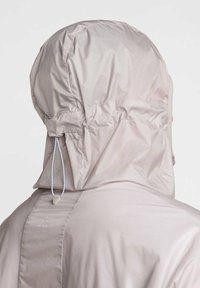 Lätt, huvad jacka i mjuk beige tyg med slät yta. Har justerbara snoddar och instoppad detalj vid huven.