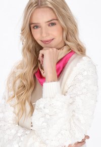 Bela kardigan s sequinom in teksturiranimi rokavi, složen nad bež topom, v kombinaciji z roza svilenim šalom z bogatim vzorcem.