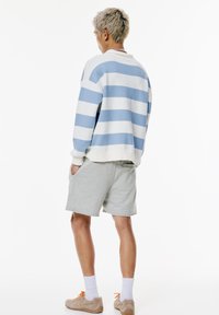 Maglione a collo alto a righe azzurre e bianche, abbinato a pantaloni corti grigi. Tessuto testurizzato con polsini a coste. Sneaker in colori neutri.