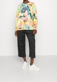 Sweatshirt coloré avec un grand graphique de Mickey Mouse, associé à un pantalon noir ample et court et des baskets blanches.