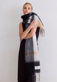 Écharpe longue multicolore présentant des nuances de gris, noir et beige, fabriquée en matériau doux avec des extrémités à franges et une étiquette portant la mention "ARCTIC FOX."