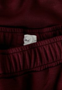 Bordo elastični pojas s nabranim detaljima, s bijelom etiketom tamnog teksta, na mekanom, laganom materijalu.