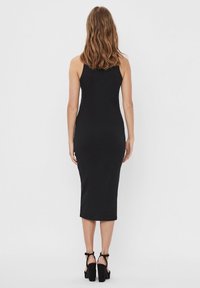 Robe midi noire côtelée à coupe ajustée avec bretelles spaghetti réglables. Le modèle porte des sandales à talons hauts noires.