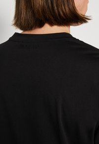 Black t-shirt featuring a crew neck and a subtle embossed logo on the back. Fabric appears smooth with a slightly relaxed fit.