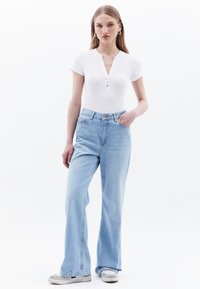 Bílý body s krátkým rukávem a henley výstřihem s třemi knoflíky, zkombinovaný se světle modrými zvonovými džíny a světlými teniskami.
