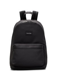 Zaino in nylon nero con una texture liscia, forma arrotondata, zip superiore e tasca frontale. Presenta un piccolo logo. Spallacci regolabili.